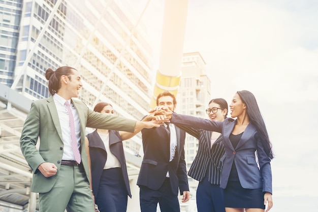 Happy young colleagues stacking hands on footpath in city