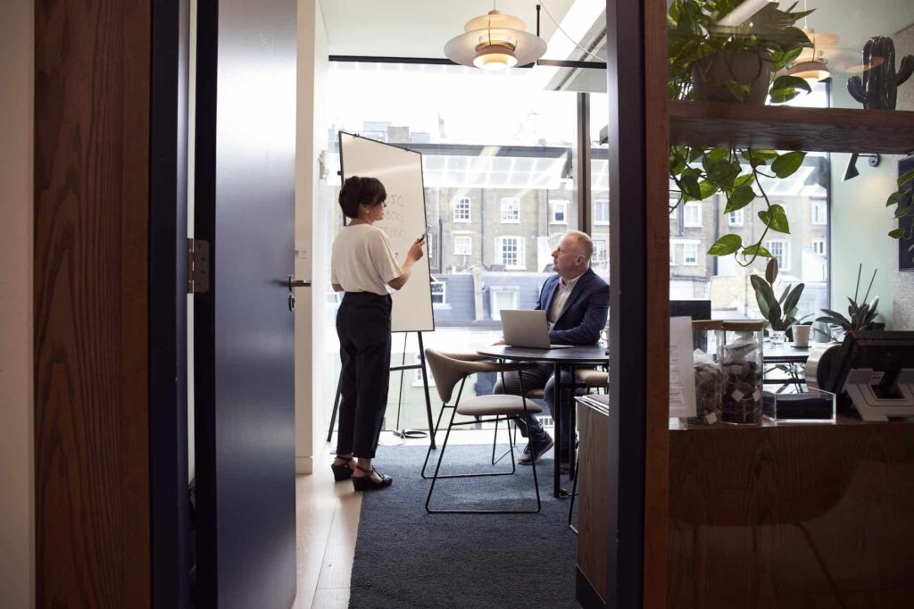 A man and woman are standing in front of a door in an office discussing it consulting services.