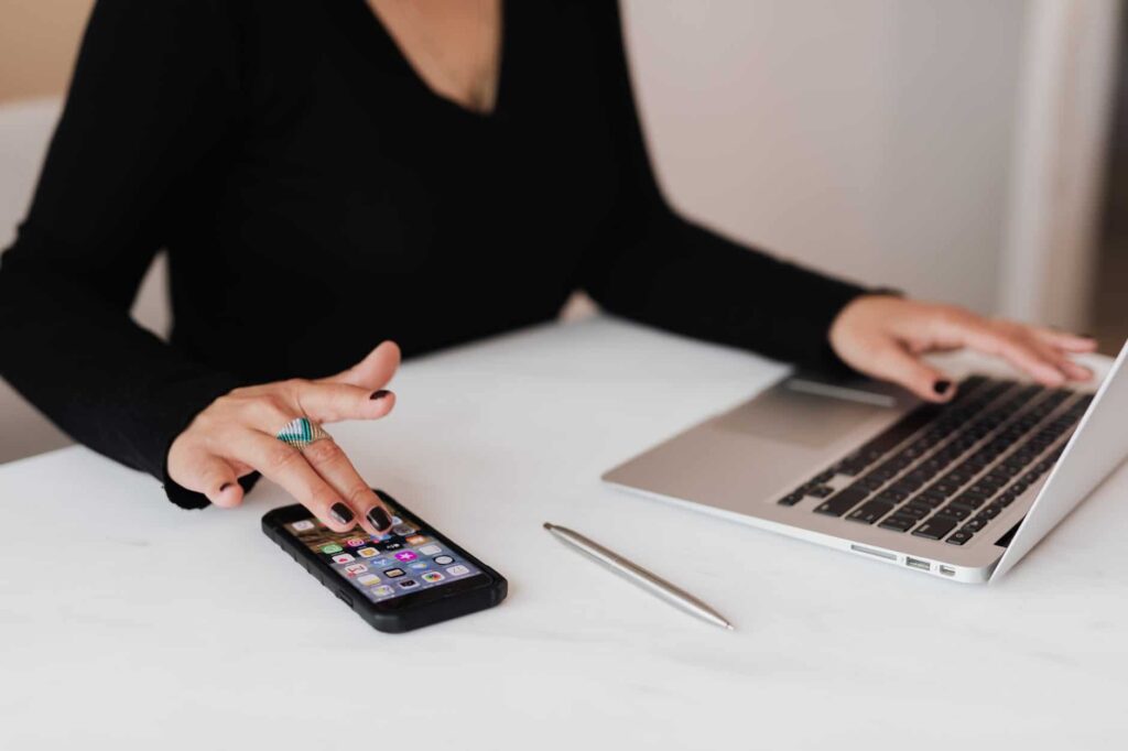 A woman using her phone and laptop on a white table, ensuring network security.