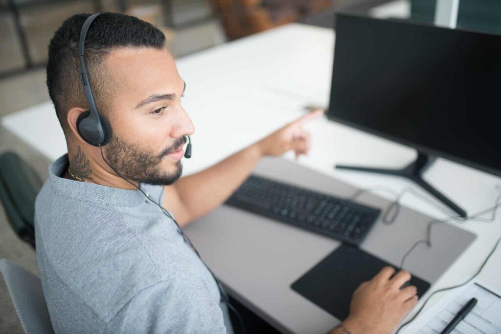 A man wearing a headset and pointing at a computer screen.